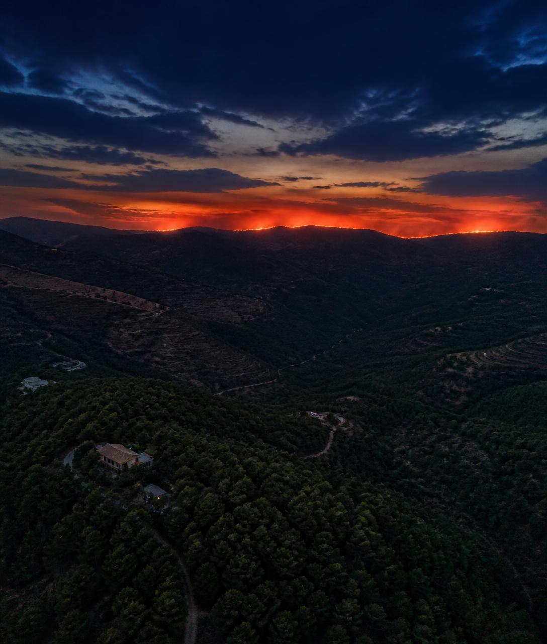 Vista aérea al atardecer de una cresta forestal en Málaga con un resplandor ámbar en el horizonte